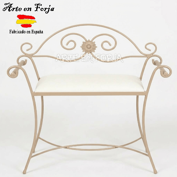 Banco descalzador de forja modelo Vélez-Blanco en hierro negro con detalle floral dorado y cojín blanco mullido en un dormitorio.